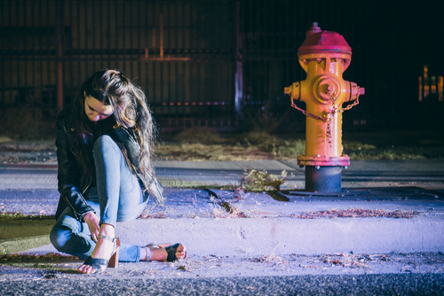 woman sitting on sidewalk at night after an auto accident where the driver left the scene