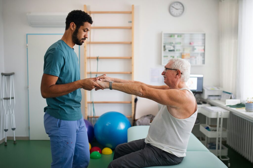 Physical therapist helping an older man with spinal injury rehabilitation exercises in a recovery clinic.