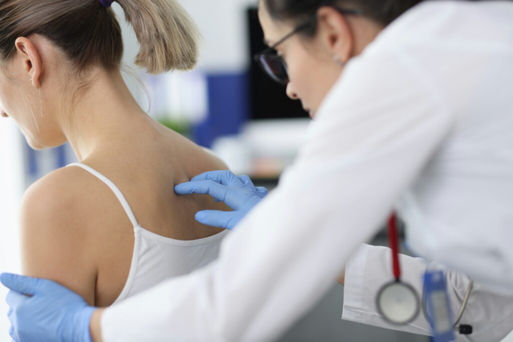Doctor examining a woman’s back during a spinal injury evaluation in a medical clinic.
