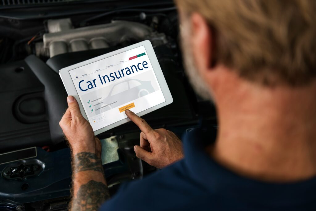 Man reviewing car insurance policy on a tablet near an open car hood