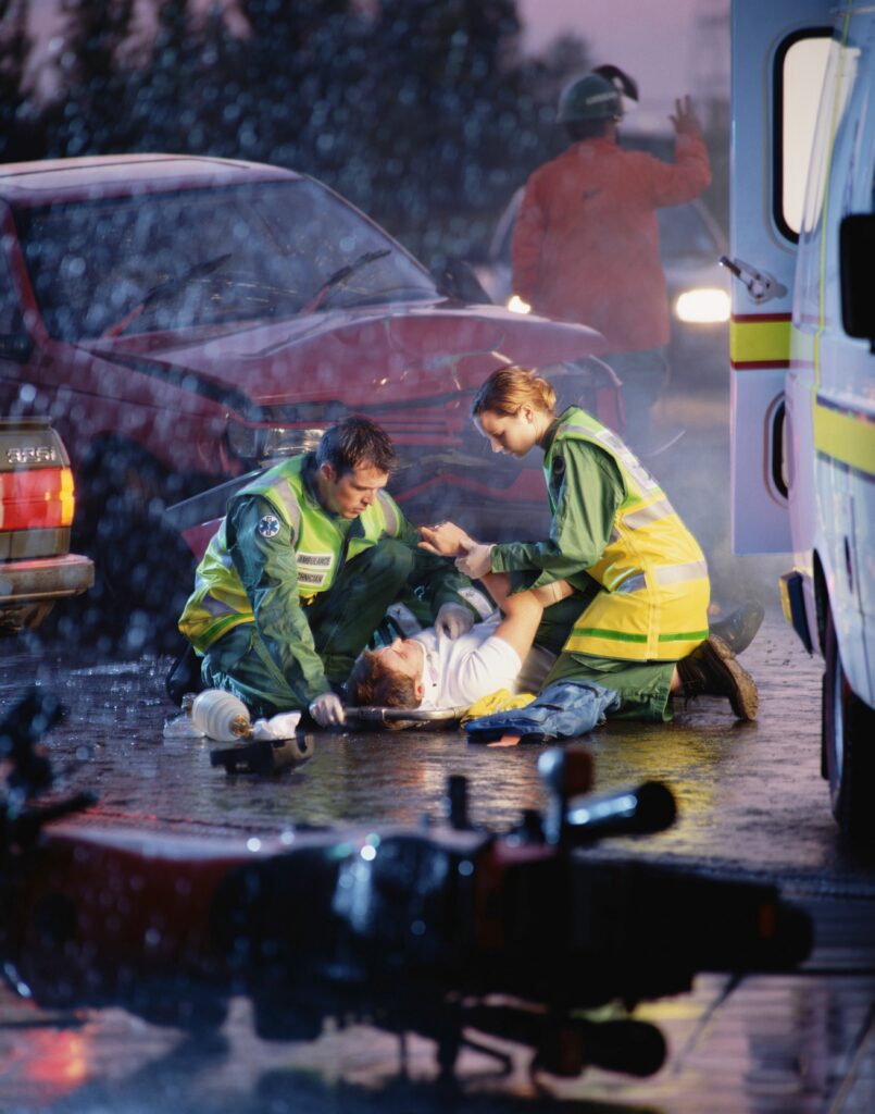 Emergency responders treating an injured person at the scene of a car accident.