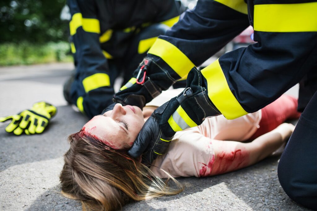 &ldquo;Emergency responders assisting an injured woman with a head wound after an accident, representing the immediate impact of traumatic brain injuries.&rdquo;