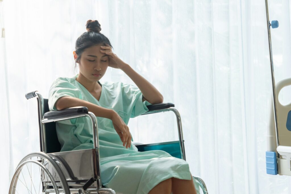 Woman in a hospital gown sitting in a wheelchair, reflecting fatigue and emotional distress during brain injury recovery.