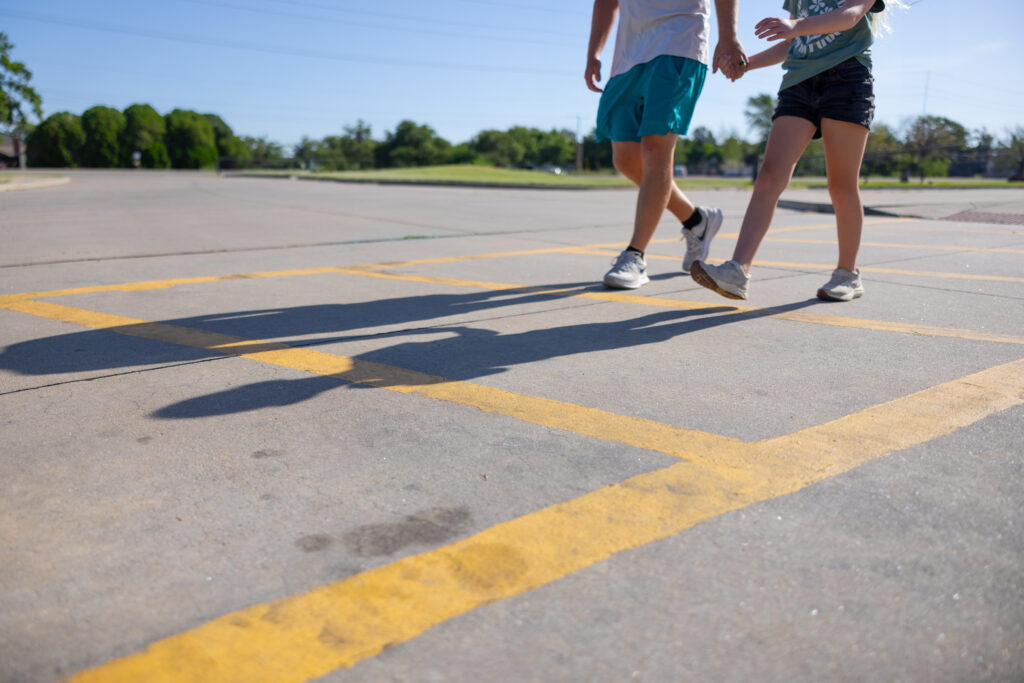 Two pedestrians walking hand-in-hand across a parking lot in Wichita, Kansas, under clear blue skies.