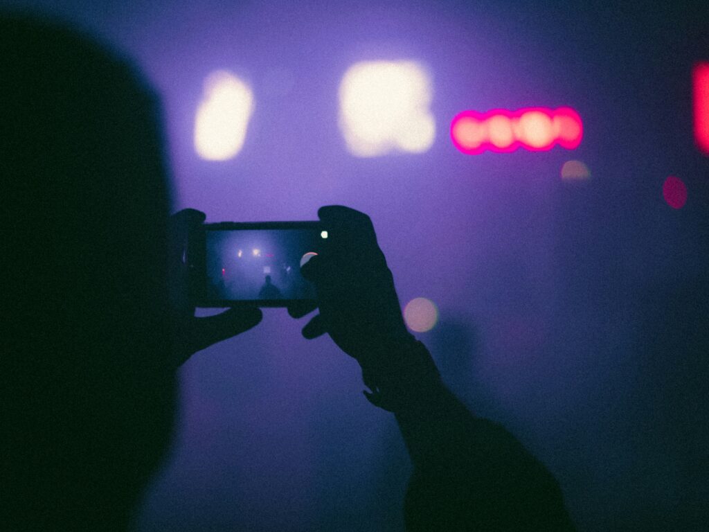 Person holding smartphone taking a photo in low light setting symbolizing social media activity
