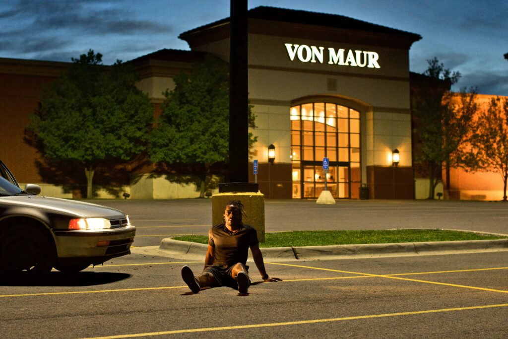 Man sitting injured on the ground in a dimly lit Wichita parking lot near a vehicle, highlighting the aftermath of a pedestrian accident.