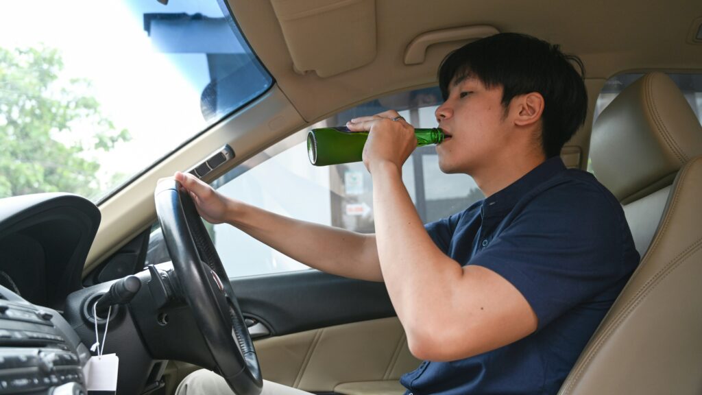 Driver drinking alcohol from a bottle behind the wheel &mdash; example of drunk driving behavior that can lead to serious car accidents.