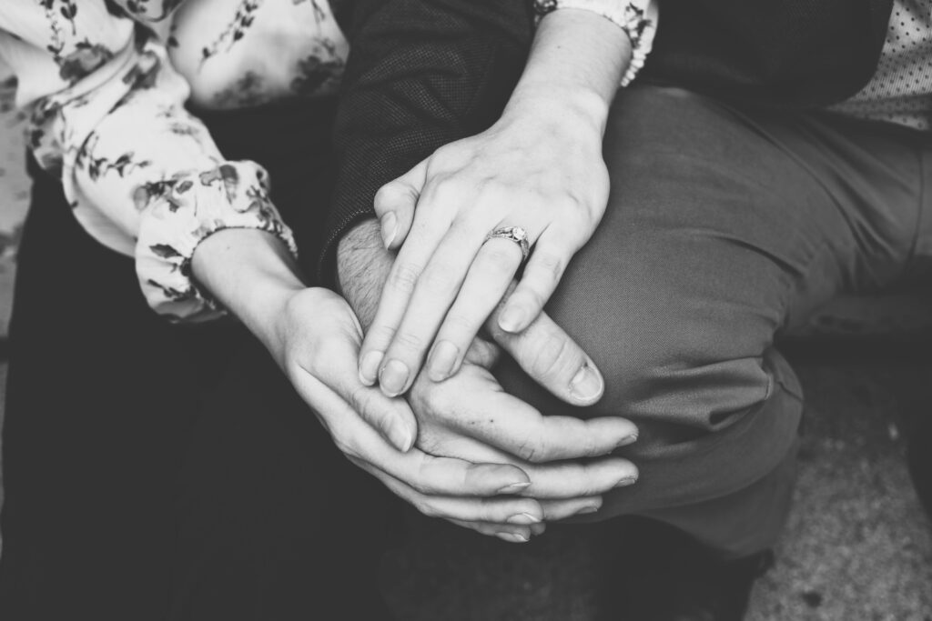 Close-up black-and-white photo of two people holding hands in comfort and support, representing empathy and togetherness during grief.