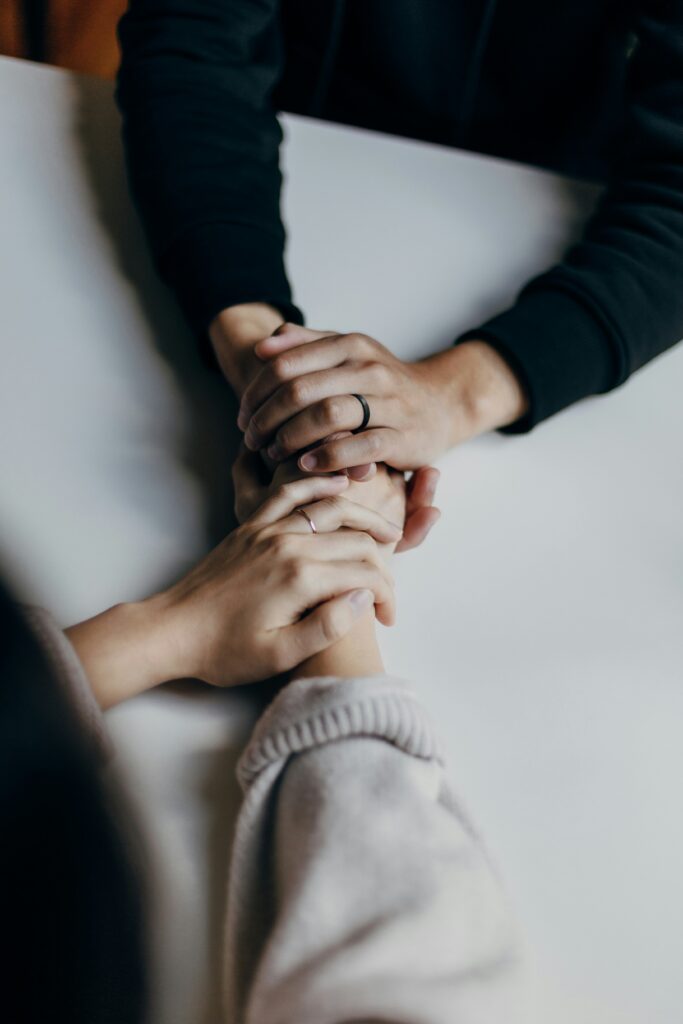 Close-up of two people holding hands across a table, offering comfort and support during a time of grief and loss.